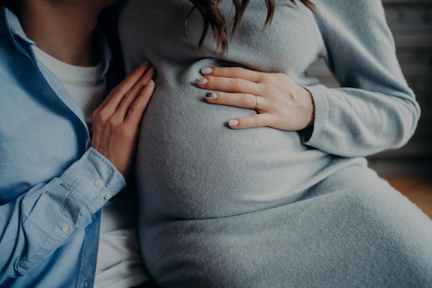 Cara de mujer embarazada mantiene las manos en la pose del vientre cerca del marido esperando al niño Concepto de familia feliz Concepto de embarazo y paternidad