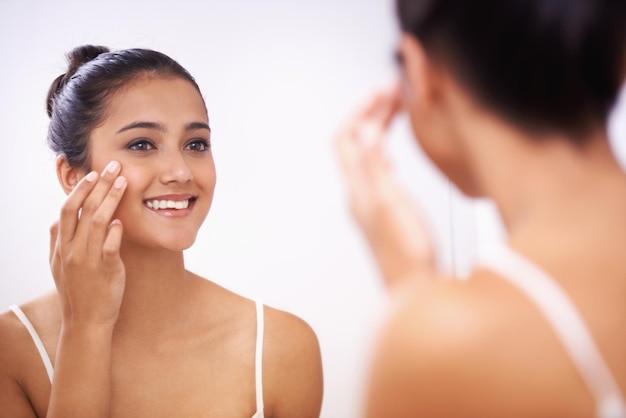 Foto cara de mujer feliz y crema en el espejo para cosméticos de belleza o maquillaje en el baño en casa persona femenina o modelo sonriendo aplicando loción o hidratante para el cuidado de la piel facial o tratamiento en el reflejo