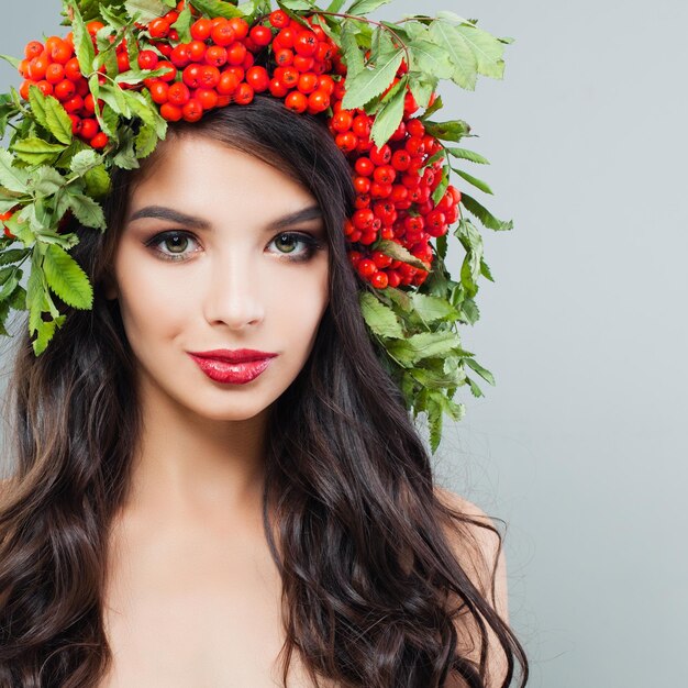 Cara de mujer joven Modelo de mujer morena con peinado largo y rizado y bayas rojas y hojas verdes en la cabeza