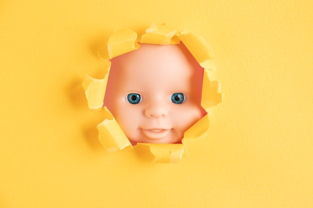 La cara de la muñeca se asoma detrás de trozos de papel amarillo, primer plano. Copie el espacio.