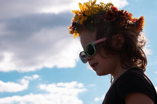 Cara de niña de 5 años con gafas de sol negras contra el espacio de copia del concepto de tiempo de verano del cielo