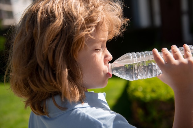 Cara de niño divertido de cerca. Niños bebiendo agua al aire libre en el parque, retrato.