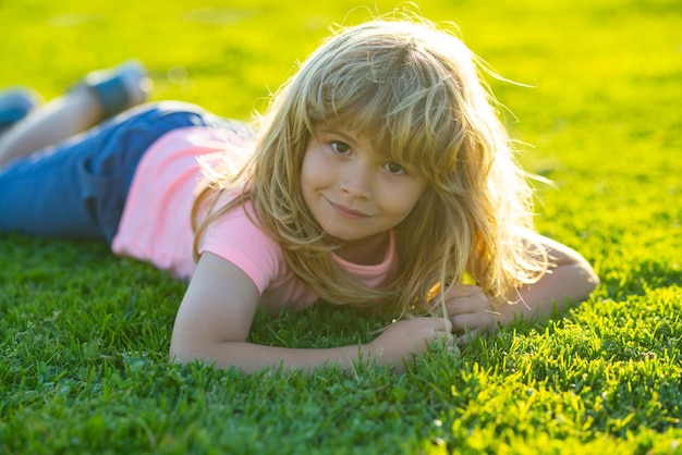 Cara de niño de primavera Niño sonriente con fondo de hierba Niño feliz tirado en la hierba en el día de la primavera Retrato de un niño sonriente tirado en la hierba verde en el parque