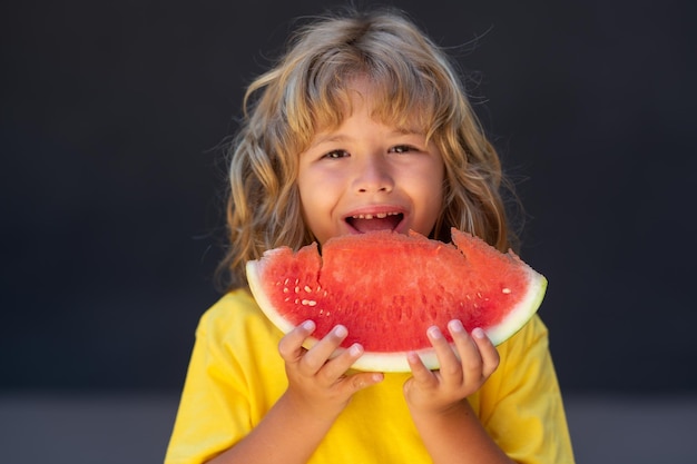 Cara de niño y sandía de cerca niño come sandía niño está recogiendo sandía sobre fondo gris