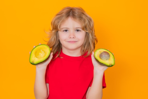 Cara de niños con frutas Niño sostiene aguacate rojo en estudio Retrato de estudio de niño lindo con aguacate aislado sobre fondo amarillo