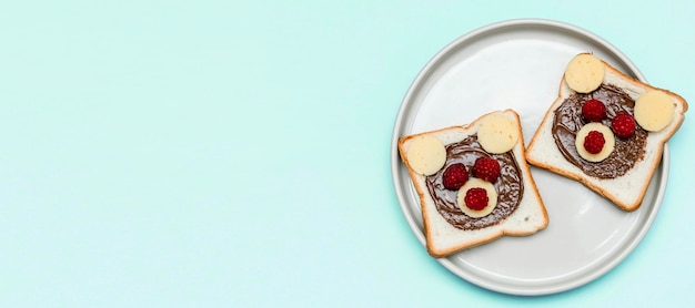 Cara de oso divertido sándwich pan tostado con queso de mantequilla de maní y frambuesa en la placa de fondo azul Niños niño dulce postre desayuno almuerzo comida cerrar