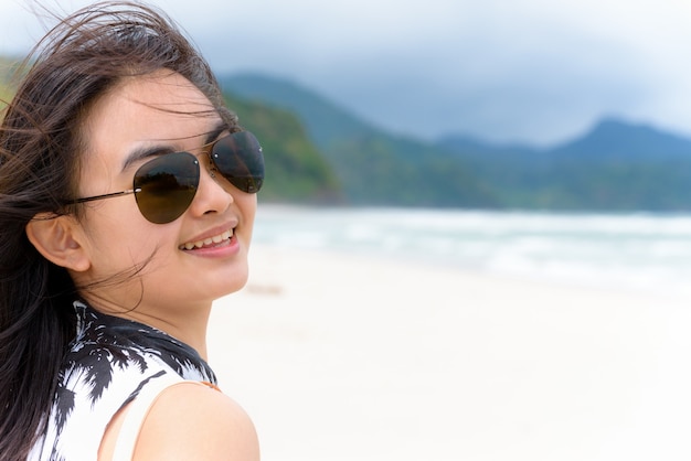 Cara de primer plano turista hermosa mujer vistiendo sunglasse mirando a la cámara y sonriendo con feliz en la playa y el mar en verano en la isla de Tarutao, Satun, Tailandia