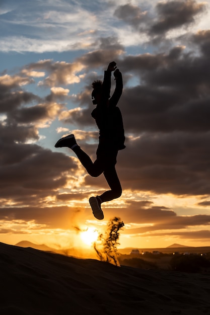Foto cara pulando na costa arenosa durante o pôr do sol
