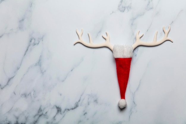 Foto cara de reno de navidad hecha de cuernos y sombrero de snata sobre un fondo de mármol