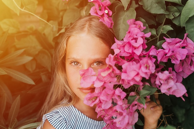 Cara de retrato de una niña pequeña y sincera de ocho años con ojos marrones en el fondo de plantas verdes y flores rosadas durante un viaje de vacaciones de verano gen z concepto de salud mental