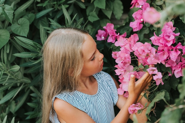 Cara de retrato de una niña sincera de ocho años sobre el fondo de plantas verdes y admirada disfrutar del olor a flores rosas durante un viaje de vacaciones de verano concepto de salud mental gen z