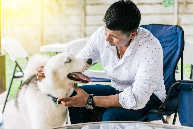 Cara sentado brincando com seu cachorro husky Jovem sentado acariciando seu cachorro no quintal Conceito de pessoa acariciando seu cachorro husky