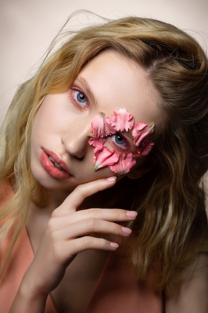 Cara seria. Modelo profesional rubia de ojos azules posando con pétalos de flores cerca del ojo