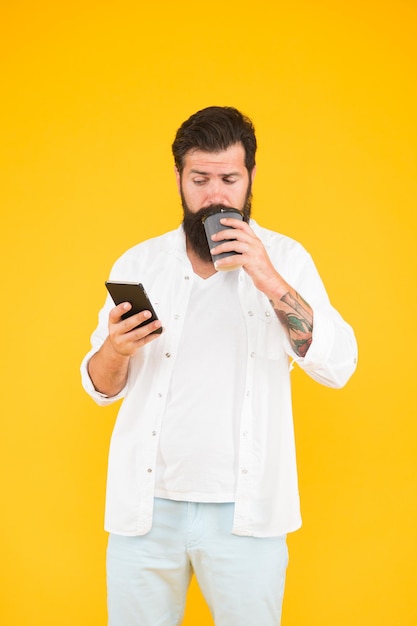 Cara sério com bigode e barba bebe café lendo bate-papo no smartphone conversando