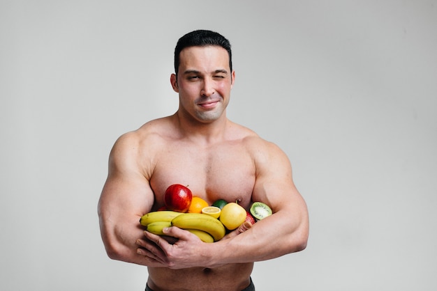 Cara sexy desportivo posando em um fundo branco com frutas brilhantes. Dieta. Dieta saudável