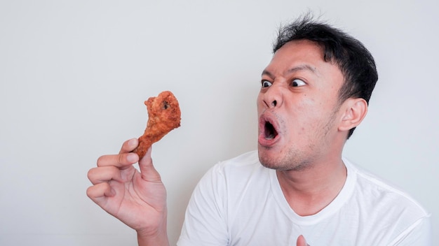 La cara de shock y Wow de un joven asiático está comiendo pollo frito con camisa blanca