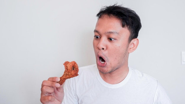 La cara de shock y Wow de un joven asiático está comiendo pollo frito con camisa blanca