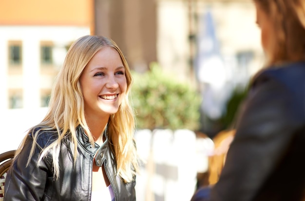 Cara sonriente y amigas hablando al aire libre en una cafetería en verano para vincularse o reunirse feliz charla o conversación con jóvenes en un café para una reunión social o ponerse al día