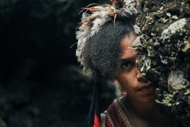 Cara sonriente de la exótica joven Papúa de la tribu Dani usando una corona de plumas en el pelo rizado escondido detrás