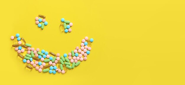 Cara sonriente forrada con pastillas brillantes en una vista superior de fondo amarillo Píldoras médicas para el cuidado de la salud