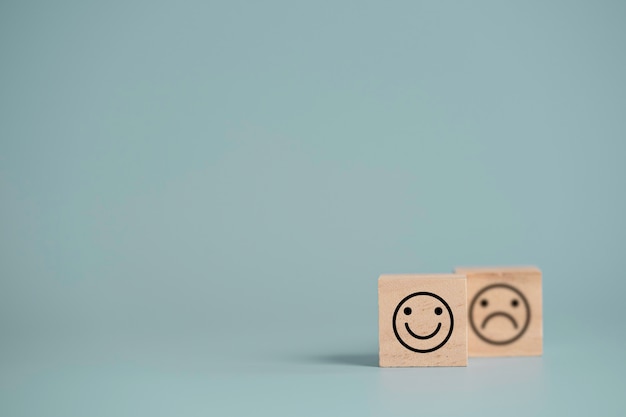 Cara sonriente frente a cara de tristeza que imprime la pantalla en un bloque de cubo de madera, selección de emociones para la satisfacción del cliente y el concepto de evaluación.