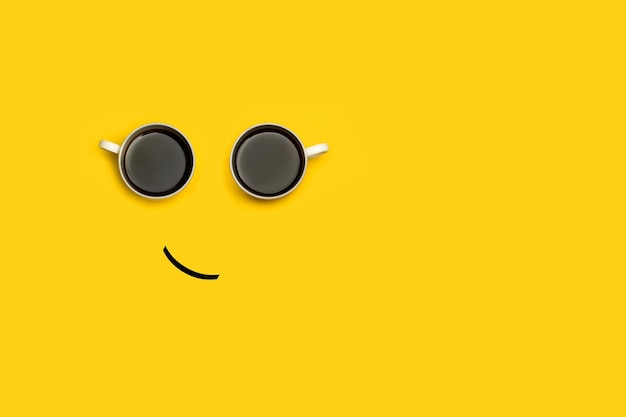 Foto cara sonriente hecha con dos tazas de café sobre un fondo amarillo