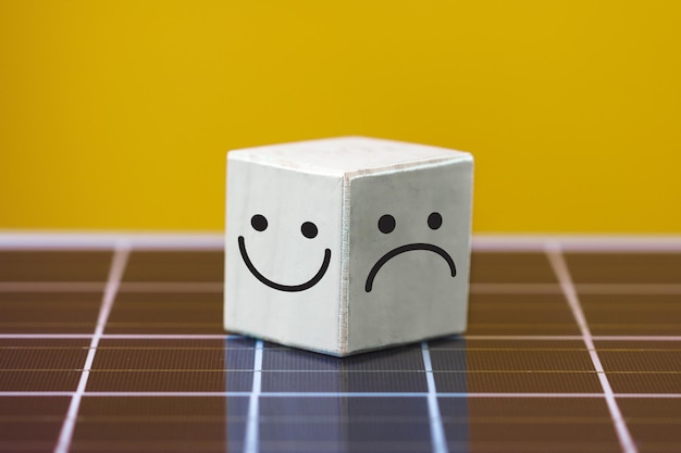 Cara sonriente en el lado brillante y cara triste en el lado oscuro en cubo de bloque de madera en panel solar fotovoltaico Mentalidad positiva concepto de energía limpia