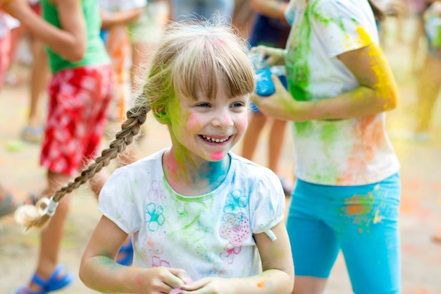 Cara sonriente de una niña con harina de colores brillantes en su rostro que se divierte en un festival callejero de colores