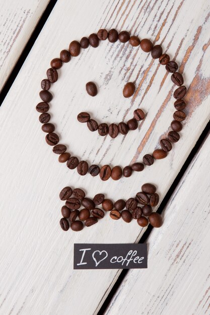 Cara sonriente con pajarita hecha de granos de café. Madera blanca en superficie.