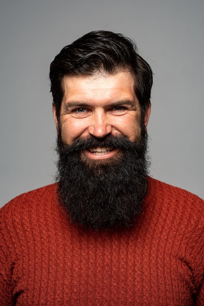 Cara de sonrisa de hombre feliz. Chico joven sonriente guapo. Peluquero con barba larga y bigote en peluquería. Hombre barbudo. Expresiones y emociones faciales humanas positivas.