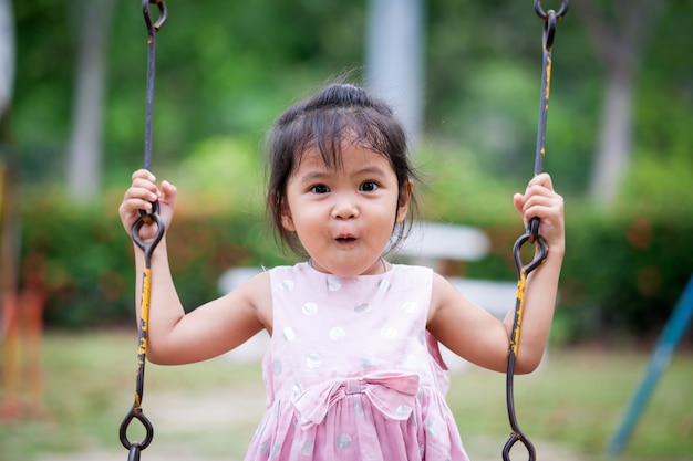 Cara sorprendida de la niña linda asiática mientras ella juega columpio en el patio de recreo