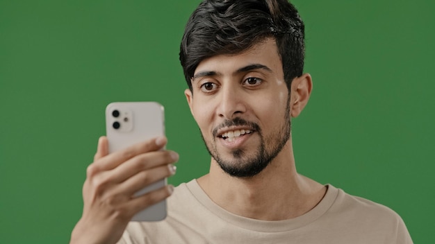 Cara sorridente árabe fazendo videochamada em fundo verde em estúdio usando o aplicativo de conferência