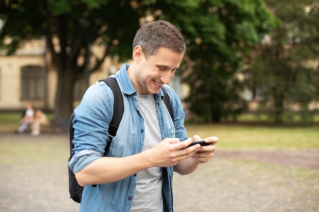 Cara sorridente com mochila jogar no telefone no videogame no parque