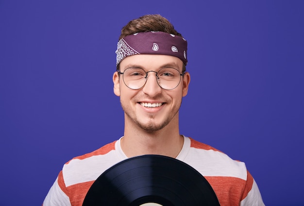 Cara sorridente de óculos, uma bandana tem um registro de música nas mãos.