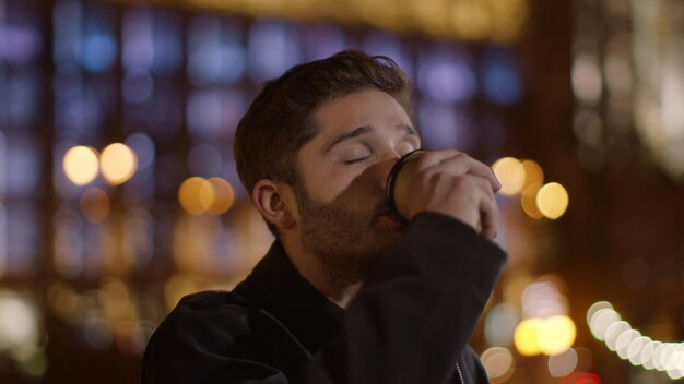 Foto cara sorridente desfrutando de café na rua escura homem feliz relaxando com copo de papel