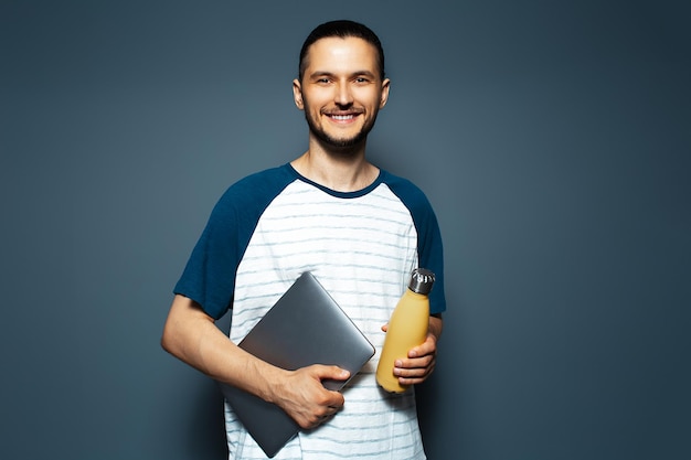 Cara sorridente segurando garrafa de água termal ecológica e laptop no fundo azul do estúdio