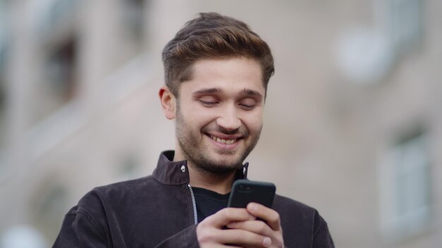 Cara sorridente usando telefone na rua Homem feliz olhando a tela do telefone do lado de fora