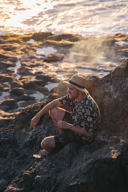 Cara sorrindo enquanto fuma sentado em uma praia vulcânica