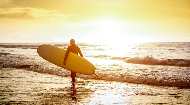 Cara surfista andando com prancha de surf ao pôr do sol em Tenerife