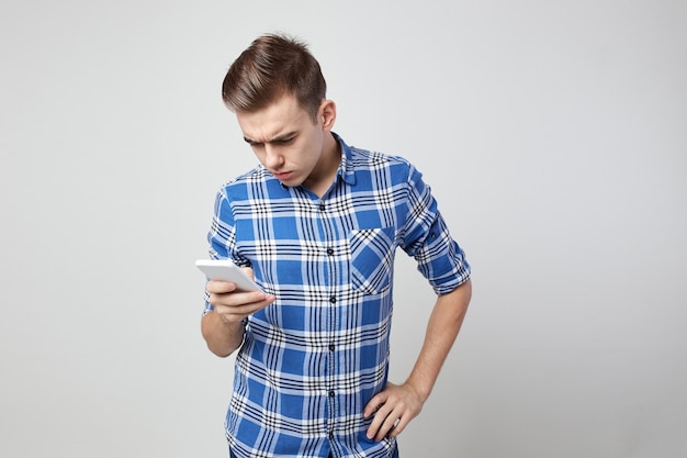 cara surpreso, vestido com uma camisa xadrez e jeans e segurando o celular