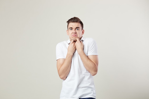 Cara surpreso vestido com uma camiseta branca e calça jeans está sobre um fundo branco no estúdio.