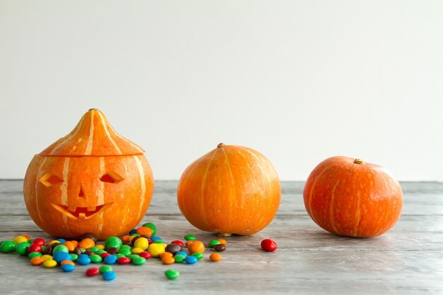 Cara tallada en calabaza con caramelo de chocolate sobre fondo de madera gris. Víspera de Todos los Santos