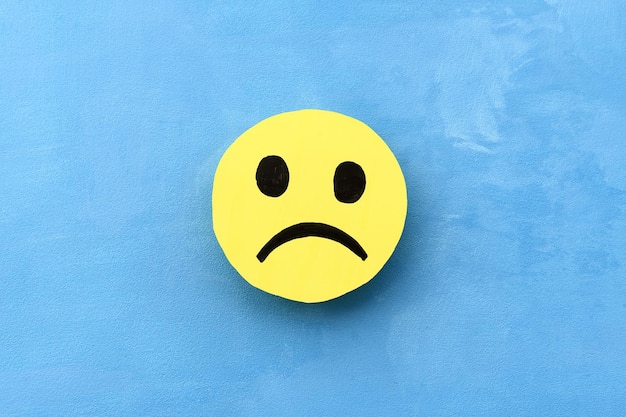 Cara triste amarela em um fundo azul O conceito de humor negativo Emoções e feedback