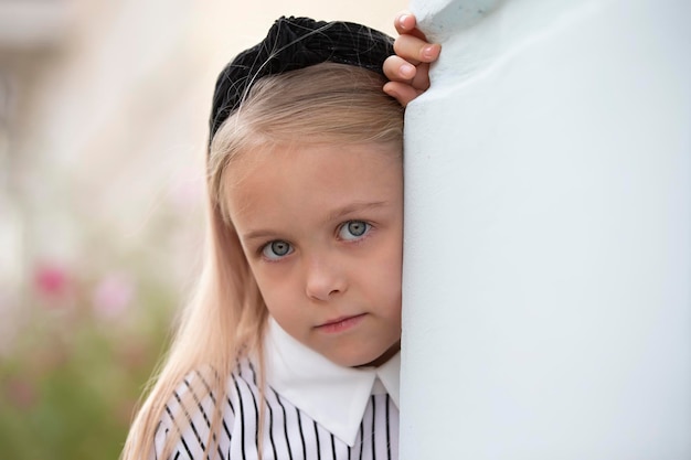 La cara triste de una hermosa niña que se asoma desde detrás de la pared.