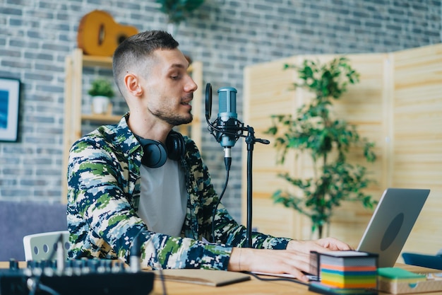 Cara usando microfone e laptop falando podcart de gravação no apartamento