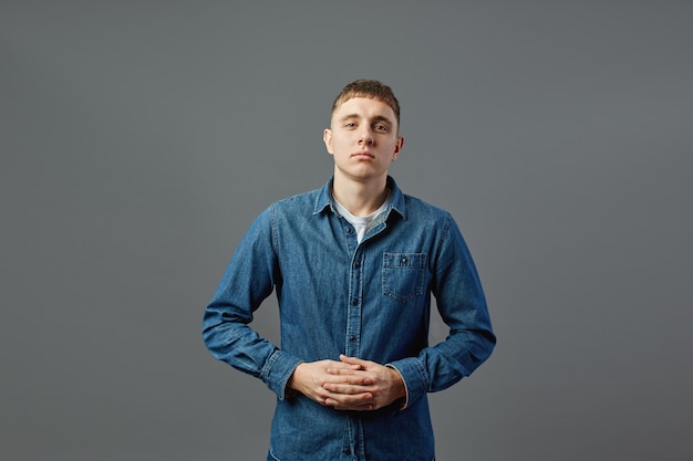 Cara vestido com uma camiseta branca, calça jeans e camisa jeans em pé com os braços cruzados no estúdio sobre o fundo cinza.