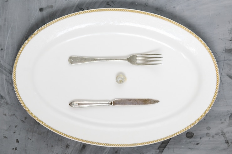 Foto caracol, tenedor y cuchillo en placa blanca sobre fondo de hormigón gris. copie el espacio.