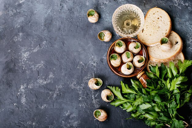 Caracoles al horno con mantequilla de ajo y hierbas frescas en una sartén, enfoque selectivo