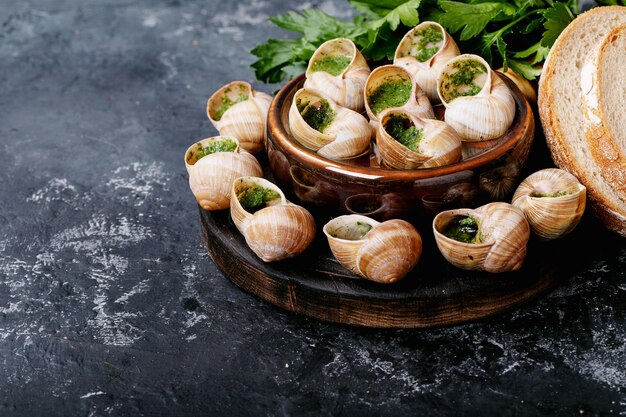 Caracoles al horno con mantequilla de ajo y hierbas frescas en una sartén, enfoque selectivo