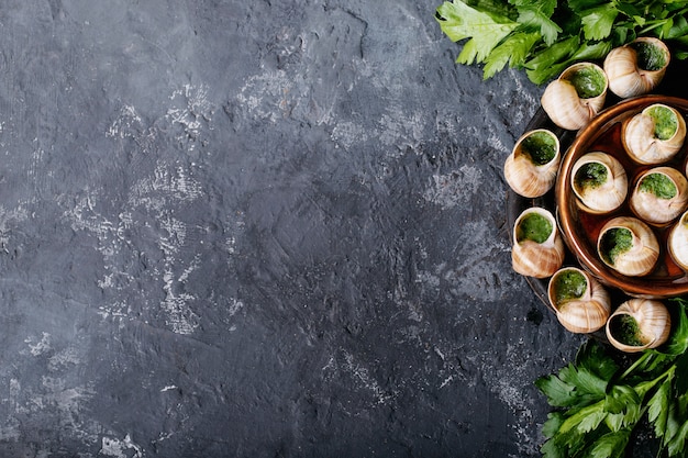 Caracoles al horno con mantequilla de ajo y hierbas frescas en una sartén, enfoque selectivo